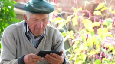 Ciddi bir yüzü olan yaşlı gri saçlı adam telefon ekranına bakıyor.. 