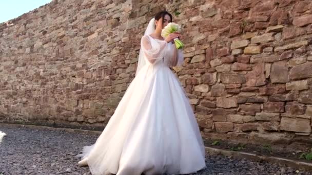 Sposa bruna in un abito da sposa bianco, porta un mazzo di fiori bianco tra le mani — Video Stock