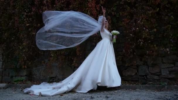 Наречена у весільній сукні дме сильний вітер, вона щиро посміхається. Щаслива дівчина — стокове відео