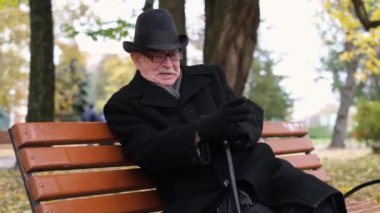 Yaşlı büyükbaba soğuk bir sonbahar gününde parkta oturuyor..