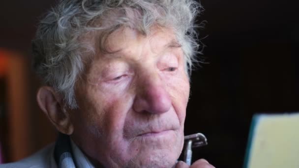 Un viejo pensionista se afeita en el espejo, se afeita las cerdas en la cara. — Vídeos de Stock