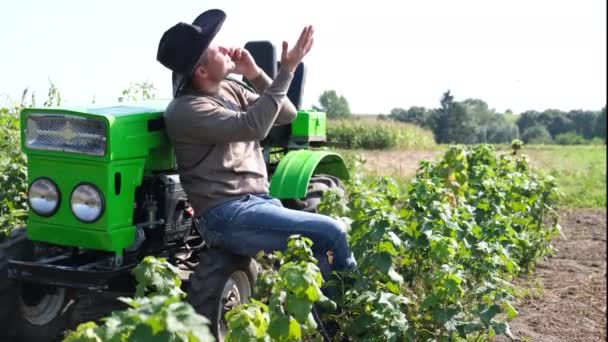 Köylü bir işçi tarlanın ortasında akıllı telefon kullanıyor, bir traktörün yanında konuşuyor.. — Stok video