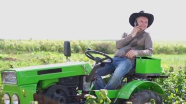 Traktör sürücüsü akıllı telefondan konuşuyor, hasat sırasında tarlada.