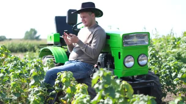 Un joven campesino está hablando por teléfono en un viñedo con un tractor cerca de él.. — Vídeos de Stock