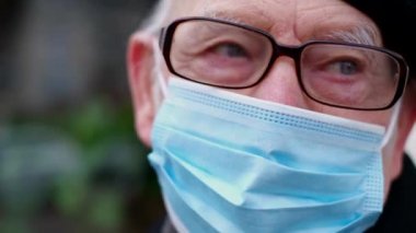 Emekli adam bir bankta oturuyor, koruyucu bir maske takıyor, virüslerden korunuyor.,