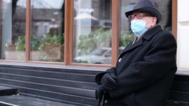 Emekli adam bir bankta oturuyor, koruyucu bir maske takıyor, virüslerden korunuyor.,