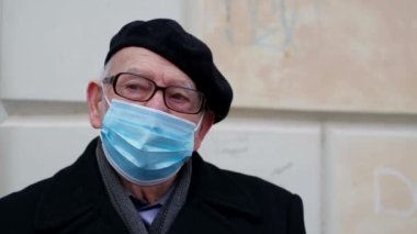 Yaşlı bir adamın portresi, gözlük takıyor ve gri saçlı, tıbbi maske takıyor.