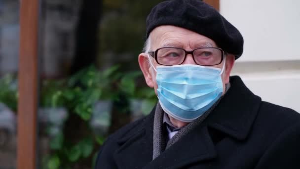 The pensioner is sitting on a bench, he is in a protective mask, protection from viruses, — Stock Video