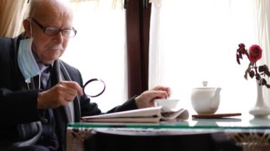 Gri bıyıklı emekli son sınıf öğrencisi mutfakta gazete okuyor.