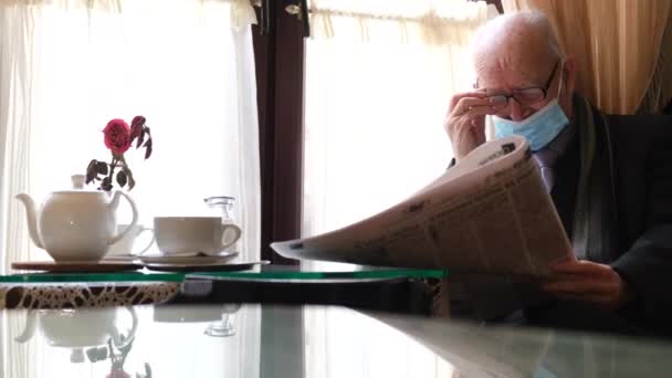 Een oude gepensioneerde met een bril zit in een café en leest een krant.. — Stockvideo