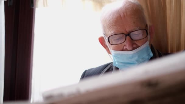 Ein alter Rentner mit Brille sitzt in einem Café und liest eine Zeitung. — Stockvideo