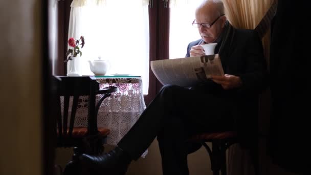 Retired senior man with gray mustache reads newspaper at home in the kitchen — Stock Video