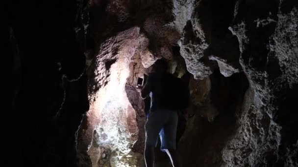 Archaeologist man shining a flashlight in a cave. Speleology, dungeons, dark tunnel — Stock Video