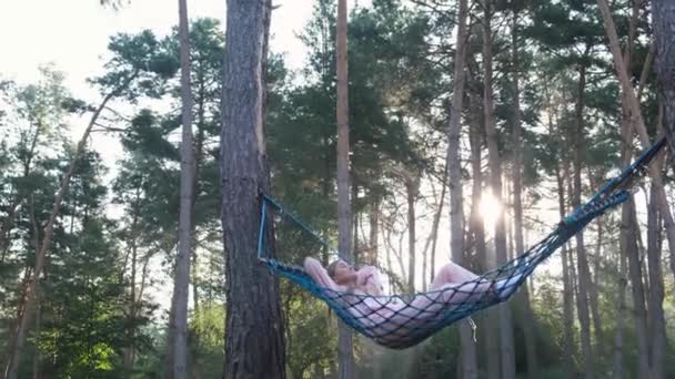 小女孩躺在松林中间的吊床上. — 图库视频影像
