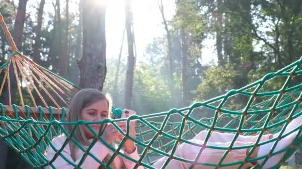 Femme se détend dans un hamac avec un smartphone dans ses mains. Vacances d'été dans une pinède. — Video