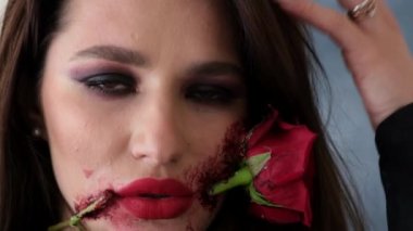 Karanlık dumanlı odada çiçekli cadı makyajlı bir kadın kameraya bakıyor.