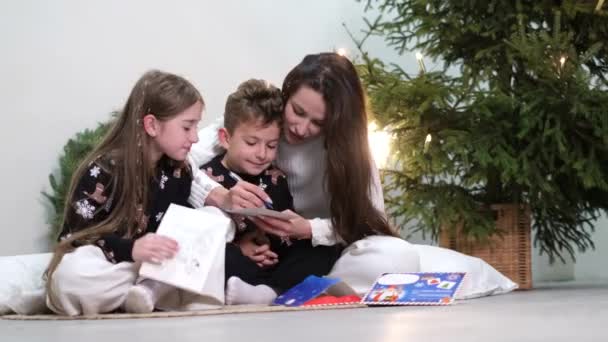 Junge Mutter mit Kindern hat Spaß und schreibt einen Brief an den Weihnachtsmann. — Stockvideo
