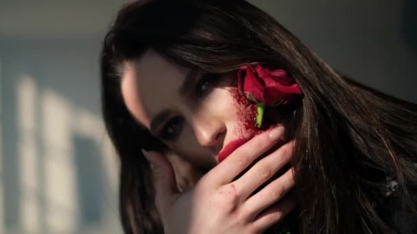 Hermosa chica con un hermoso maquillaje de arte en su cara, ella tiene una flor de rosa en su boca. — Vídeos de Stock