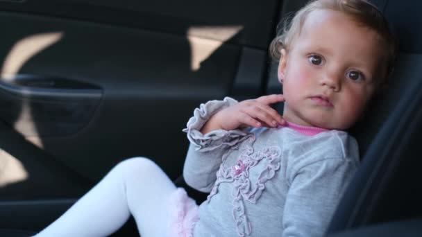 Un petit enfant est assis dans la voiture, elle regarde attentivement. — Video