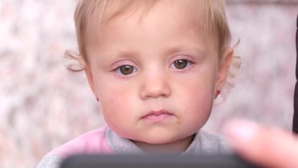 Little girl close up, she looks closely at the smartphone. The girls face. — Stock Video