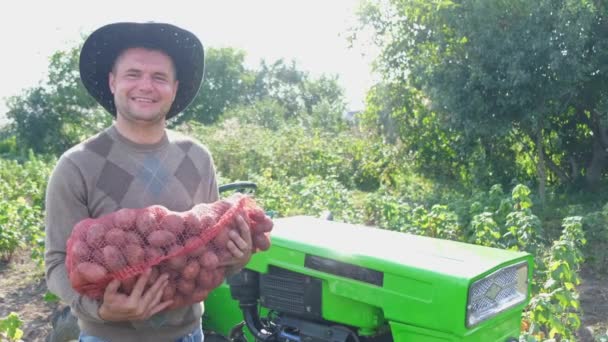 L'agriculteur inspecte la récolte de pommes de terre sur le fond d'un tracteur vert. Cultiver des légumes — Video
