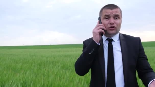 Egy mezőgazdász egy zöld mező közepén, egy okostelefonon beszél üzleti ruhában. — Stock videók