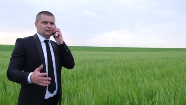 Un hombre con un traje de negocios está hablando en un teléfono inteligente en medio del campo. Empresarios discutiendo — Vídeos de Stock