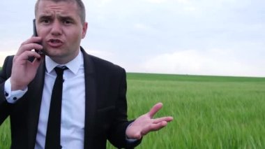 Sinirli iş adamı, sahada akıllı telefondan konuşuyor. Siyah takım elbiseli adam.