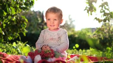 Bahçedeki yeşil çimlerin üzerinde oturan küçük kız. Çocuğun elinde kırmızı viburum var.. 