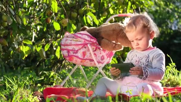 Niño europeo jugando cerca del cochecito, ella está sentada en la hierba verde en el jardín. — Vídeo de stock