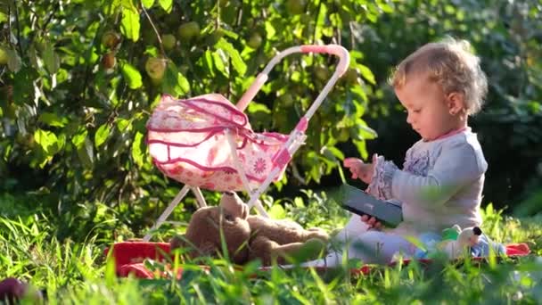 Bonne petite fille assise sur l'herbe verte. L'enfant joue à la maternelle. Bébé sourire — Video