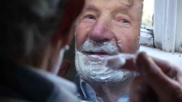 Kakek tua berambut abu-abu menerapkan busa ke wajah untuk mencukur dan melihat di cermin — Stok Video