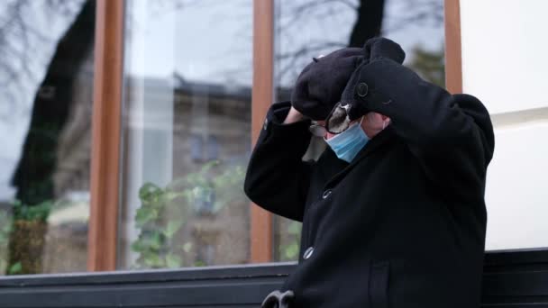 Der Senior sitzt während der Quarantäne auf einer Bank in der Stadt. Opa mit Schutzmaske — Stockvideo