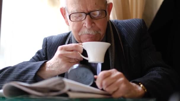 Šedovlasý dědeček sedí v kavárně a pije čaj, čte noviny.. — Stock video