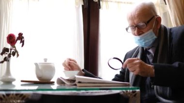 Gri saçlı büyükbaba bir kafede oturmuş çay içiyor ve gazete okuyor.. 