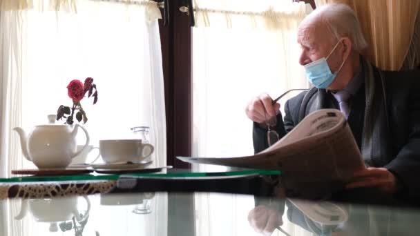Um velho grisalho lê um jornal e bebe chá num café.. — Vídeo de Stock