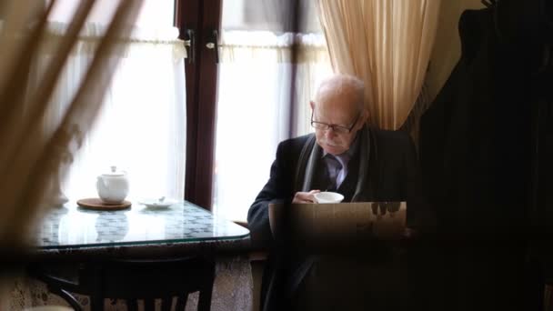 Old grandfather reads the press while sitting in a cafe. The pensioner is resting — Stock Video