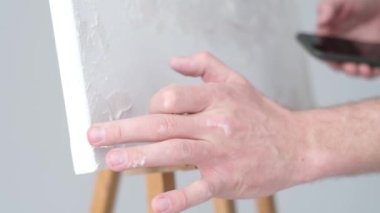 Genç yetenekli ressam büyük beyaz bir tuvale resim yapar, renkli, elle tutulur bir yağlı boya resim yapar.