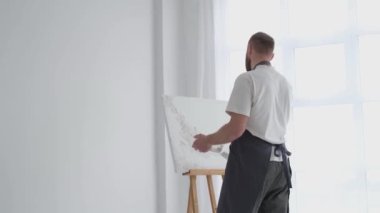 Erkek sanatçı, stüdyoda çalışırken yağlı boyalarla resim yapar.