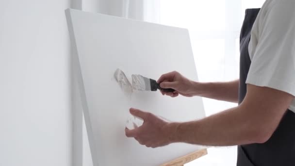 Der junge talentierte Künstler malt auf einer großen weißen Leinwand, schafft ein buntes, greifbares Ölgemälde — Stockvideo