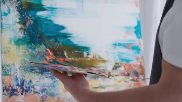 Artista masculino pinta un cuadro con pinturas al óleo, artista mientras trabaja en el estudio — Vídeos de Stock