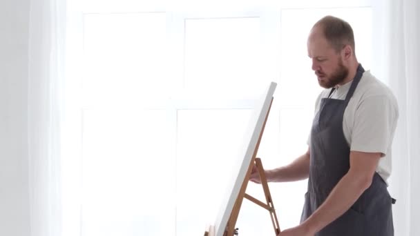 Mladý talentovaný umělec maluje na velké bílé plátno, vytváří barevnou, hmatatelnou olejomalbu — Stock video