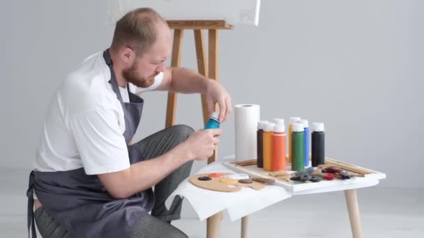 Junger Künstler, der im Atelier vor einer Leinwand arbeitet, ein Bild malt, glücklicher moderner Künstler — Stockvideo