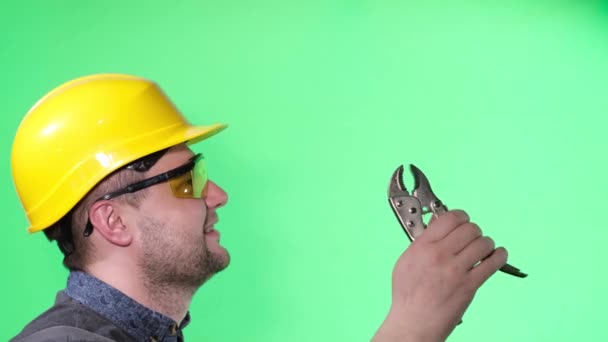 Engineer worker holding pliers on green background, he looks to the side — ストック動画