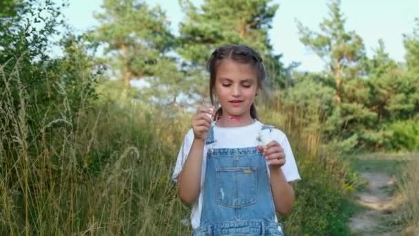 Little girl blowing soap bubbles in a city park. Child plays with soap bubbles of nature. — Stockvideo