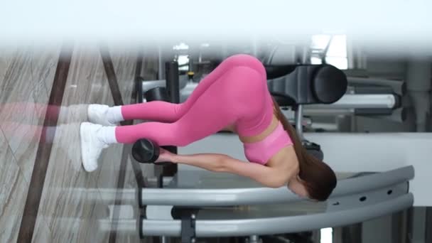 Vacker flicka gör övningar i gymmet, hon bär en rosa kostym. Vacker atletisk figur — Stockvideo