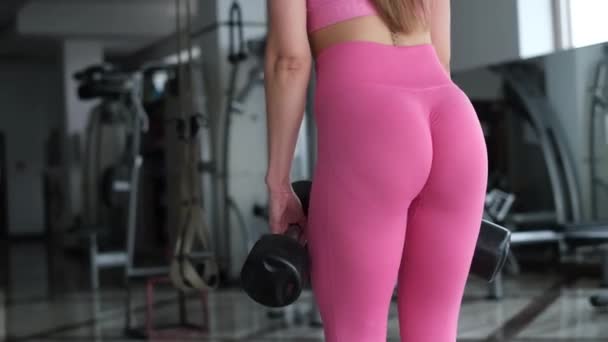 The girl in the gym she lifts dumbbells, she wears a pink suit. — Wideo stockowe