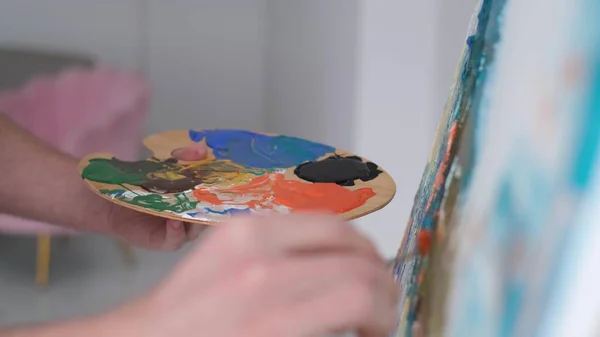 Foto ravvicinata di una mano di un artista che tiene un pennello e disegna un quadro con vernice multicolore. — Foto Stock
