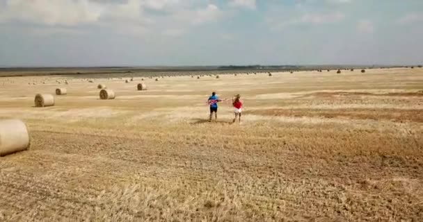 Una giovane coppia felice corre spensierata e salta su un campo di grano. Portare la bandiera USA — Video Stock