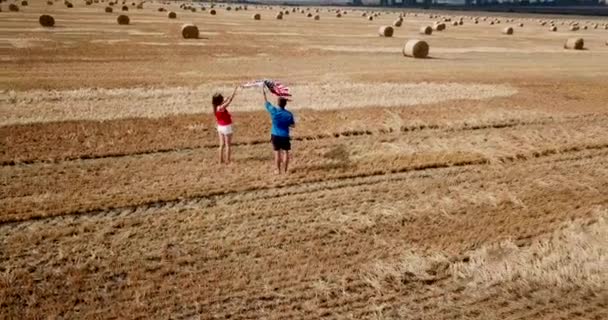 Una giovane coppia felice corre spensierata e salta su un campo di grano. Portare la bandiera USA — Video Stock